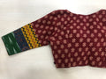 A 3/4 sleeve multicolor cotton blouse from VIKA Boutique, featuring intricate floral patterns and a unique maroon design accented with green, yellow, and black geometric prints, is laid on a light wooden surface.